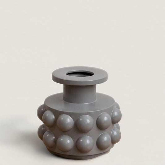 A contemporary grey vase with raised circular details displayed on a bright white backdrop showing its sculptural form in a clean simple setting.