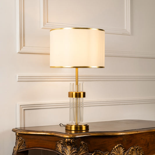 Gold metal table lamp with fabric drum shade offering sophisticated modern decor and warm ambient lighting indoors.
