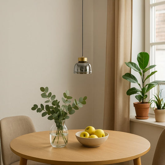 Smoked glass pendant light with gold metal top hanging above a wooden dining table styled with plants and natural light.