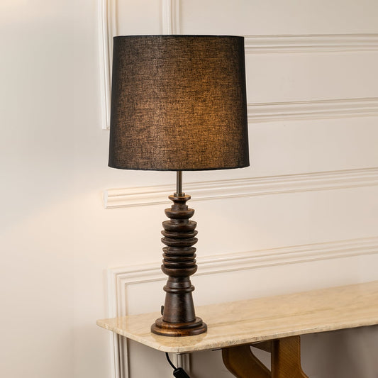 Black fabric shade table lamp with turned wood base casting warm ambient light for elegant bedside table decor.