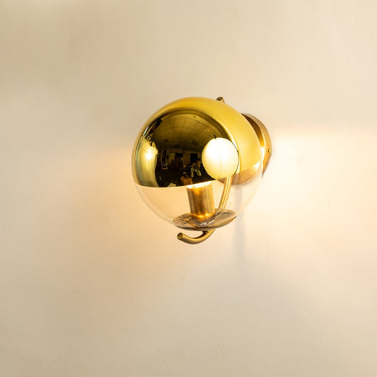 A gold metal and glass wall light shining warmly on a smooth white background creating gentle ambient illumination and adding luxurious modern décor.
