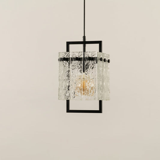 Pendant light with a textured glass shade framed in black metal glowing warmly and creating an elegant patterned illumination that adds a refined modern accent to the interior.