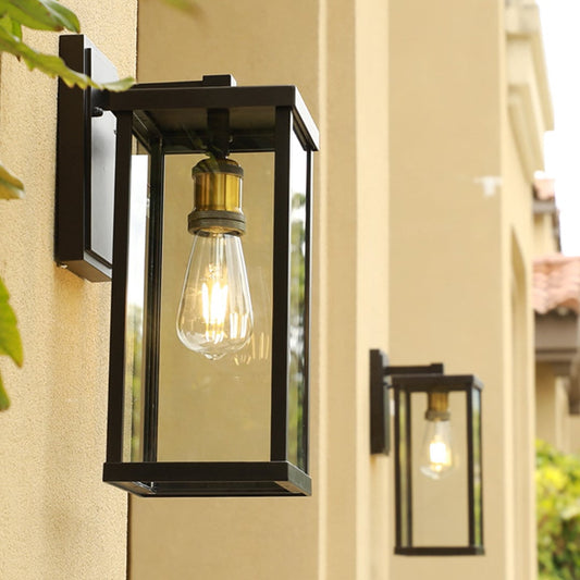Outdoor wall light with black metal frame and glass shade glowing warmly on beige exterior wall for home entrance decor.