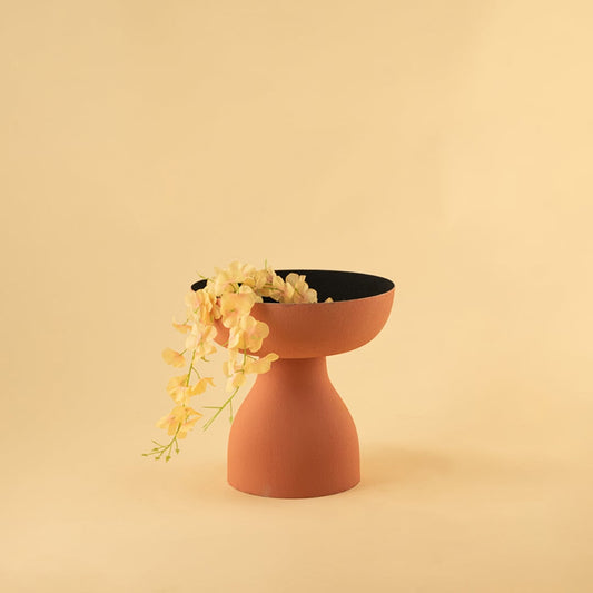 Terracotta orange pedestal bowl with black interior styled in a modern home setting adding warm artistic decor to shelves and tables.