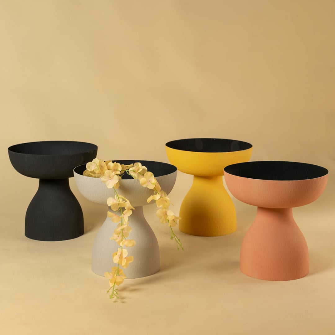 Yellow decorative pedestal bowl with black interior shown in a curated group setting for modern artistic home styling.