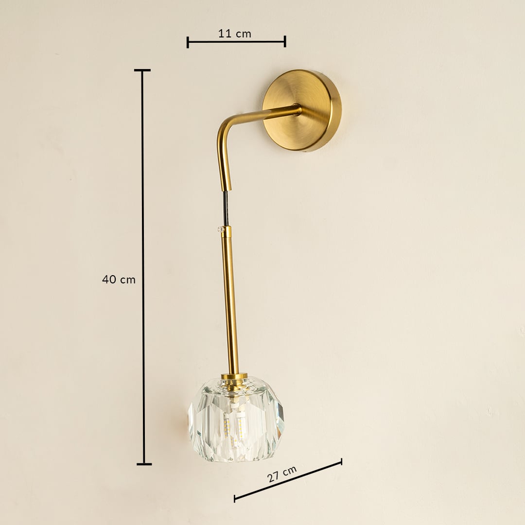 A sleek gold wall lamp with a crystal shade displayed with lights off against a dark background showcasing its modern design and metallic finish.