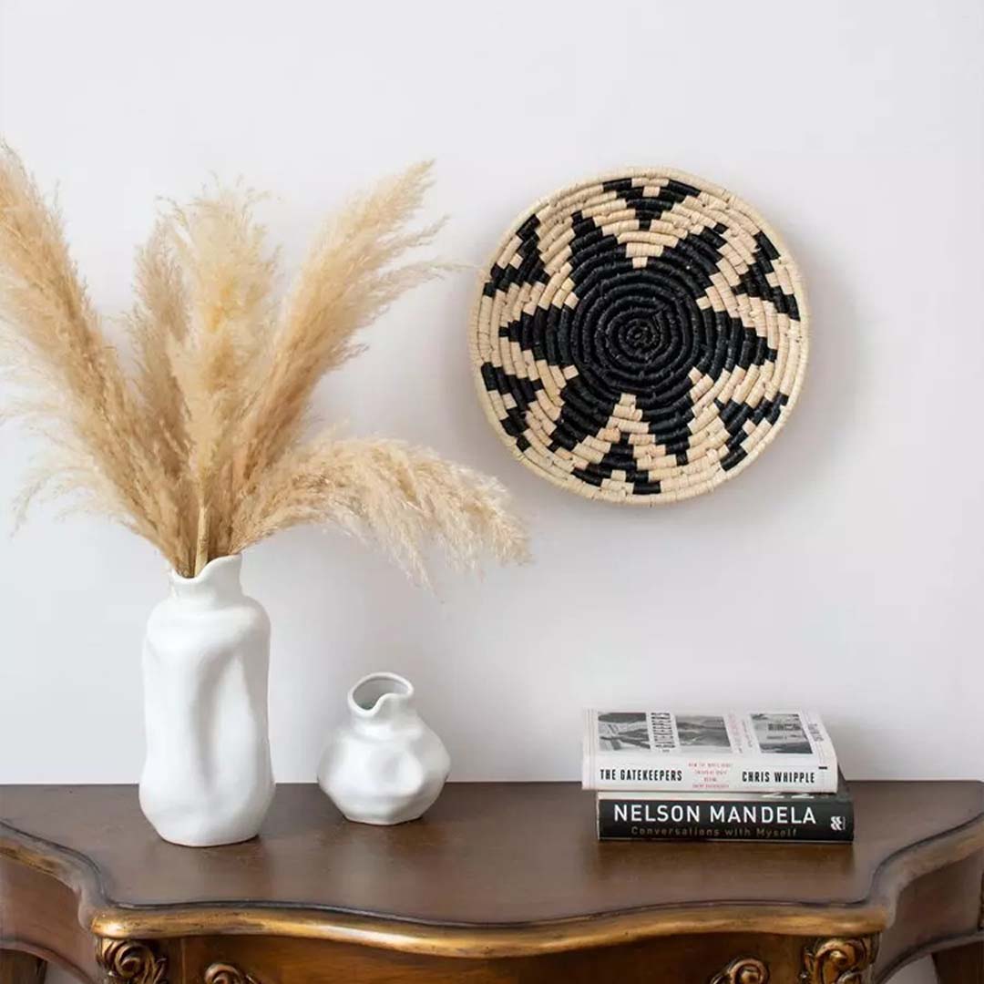 Black star handwoven wall basket styled above a wooden console with pampas grass in a ceramic vase adding a touch of artisanal charm and earthy elegance to the living space décor.