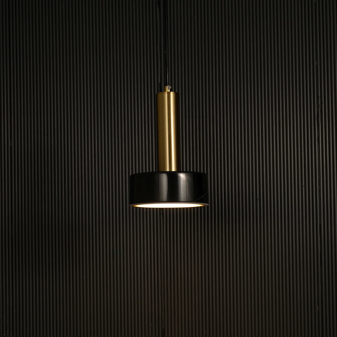 Black marble and metal round base pendant light hanging against dark textured wall with light off for luxury interior décor.