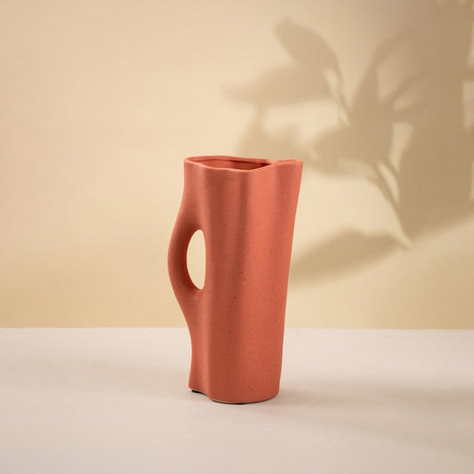 Contemporary terracotta ceramic vase with matte surface and sculpted handle-style cutout placed on a plain white background.