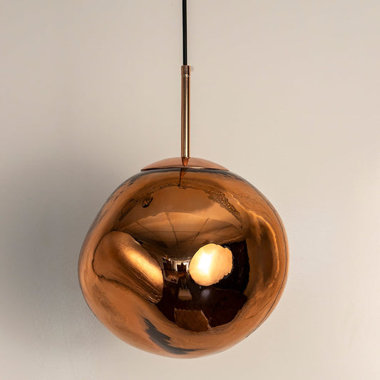 Amber glass globe pendant light turned off with rich golden hue and reflective surface shown against a white background.