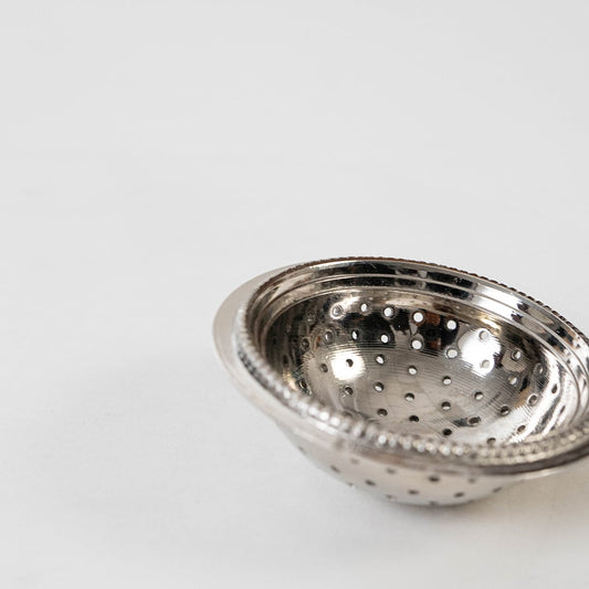 Detailed closeup view of the perforated holes and beaded rim design on the silver tea strainer head on a white background.