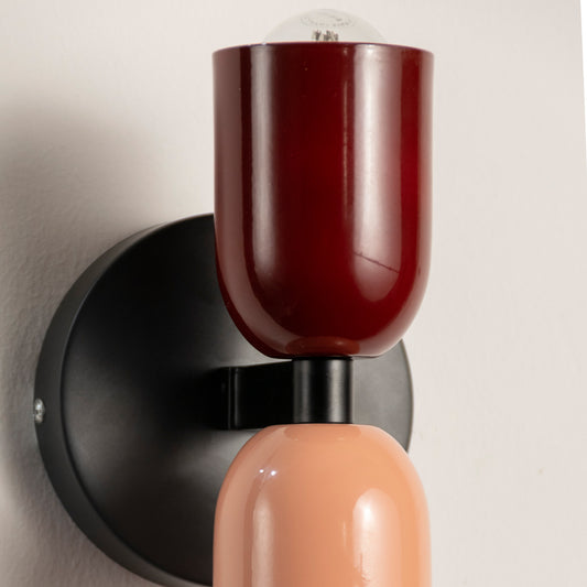 Closeup of burgundy metal wall light with peach glass shade for modern interior lighting and home décor styling.