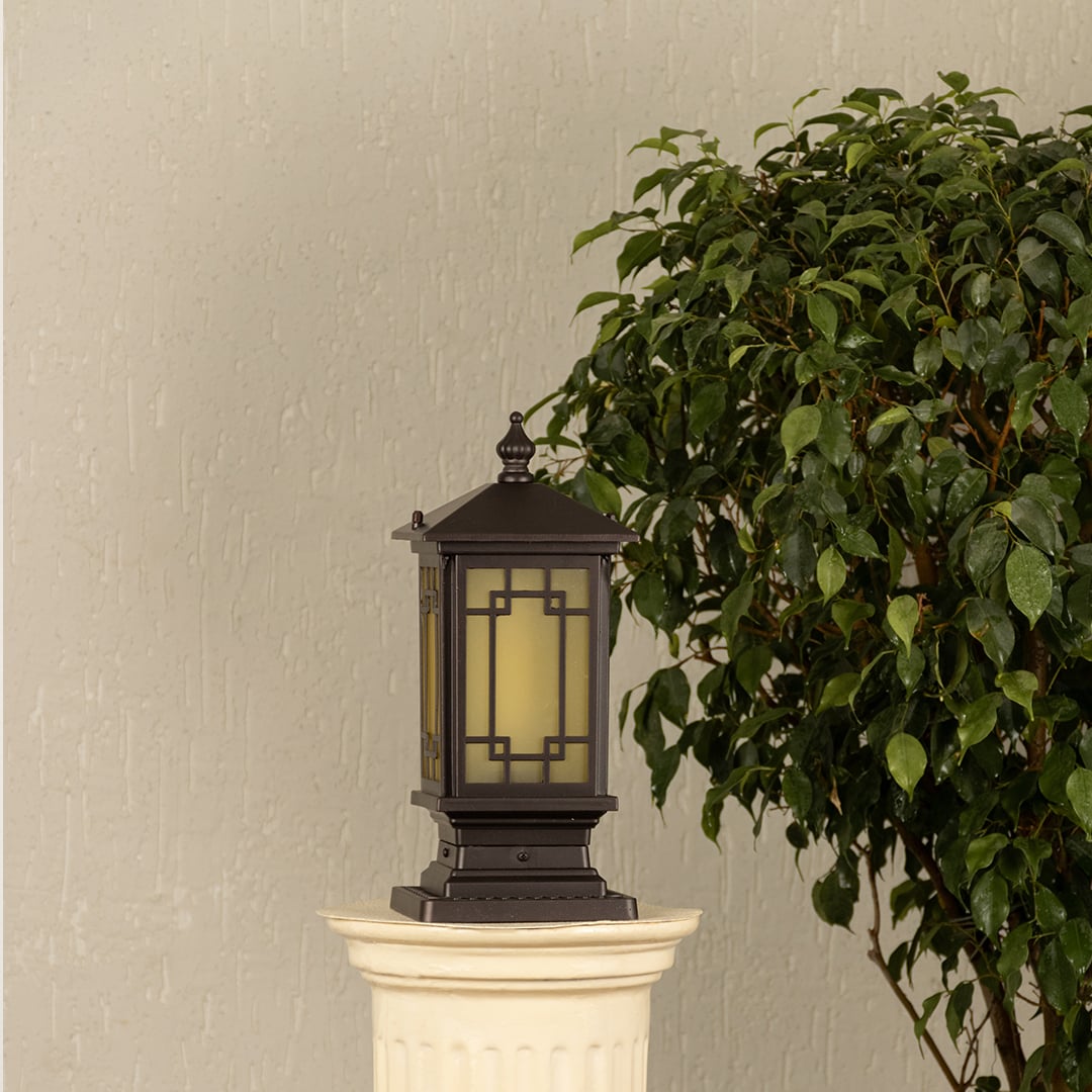 Black post light ribbed glass Light On placed next to a large green plant Lifestyle image for patio decor.