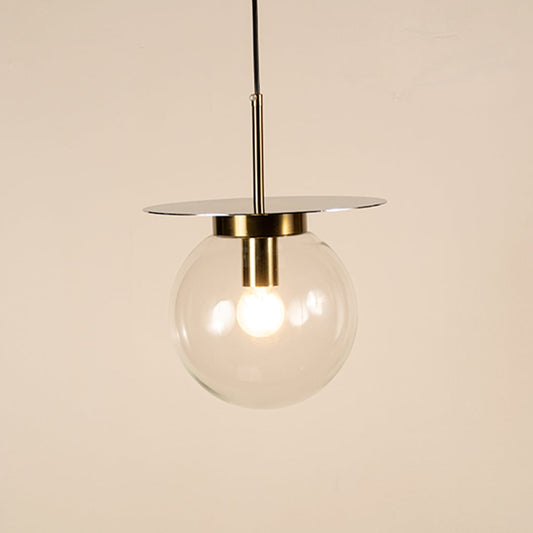 Clear glass pendant light with gold holder glowing softly on white background creating modern ambience for modern living and dining rooms.