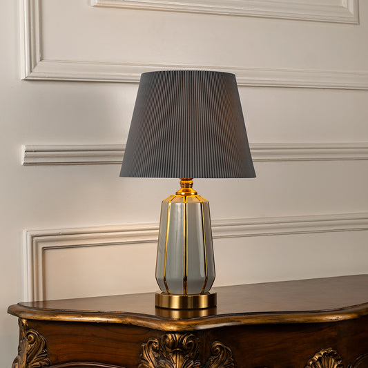 Gold metal table lamp with grey pleated fabric shade adding sophisticated ambient lighting and luxury decor appeal.