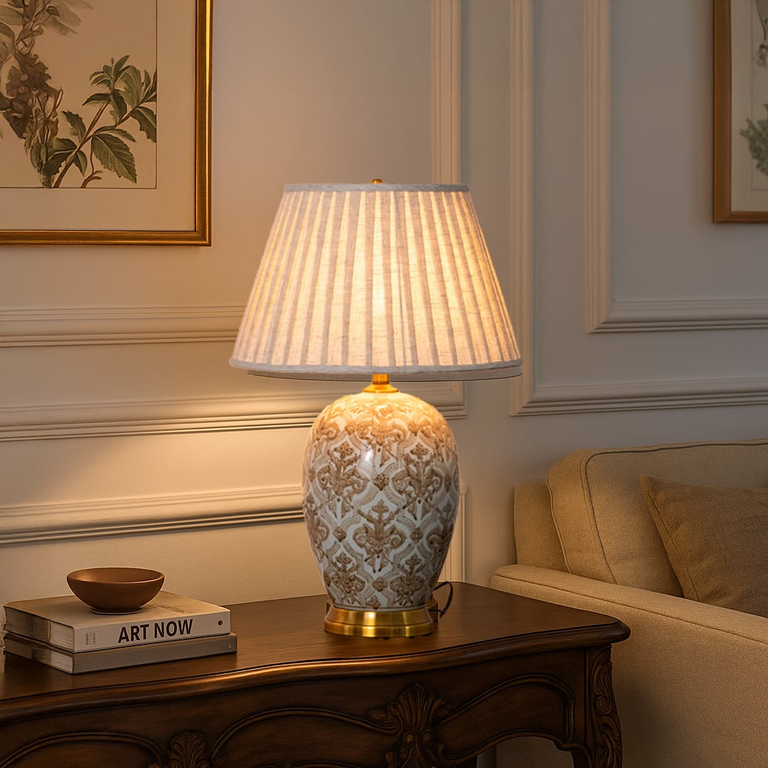 Elegant ceramic table lamp with gold base and pleated beige shade styled on wooden side table in living room decor.