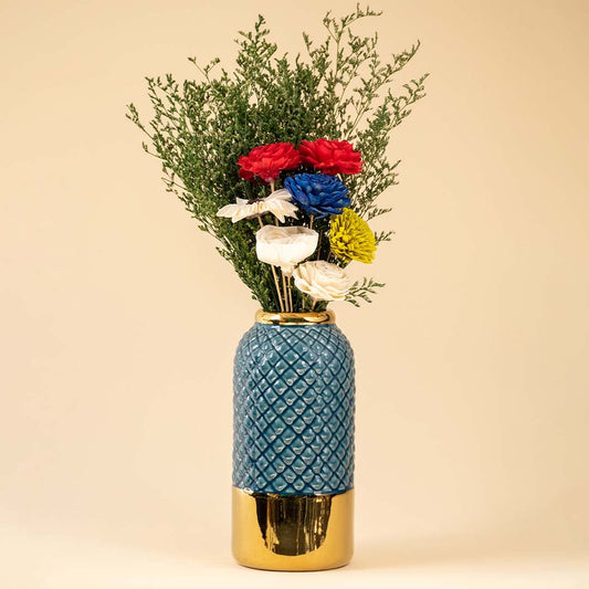 A blue patterned vase with vibrant mixed flowers displayed against a warm interior background creating a soft decorative accent.