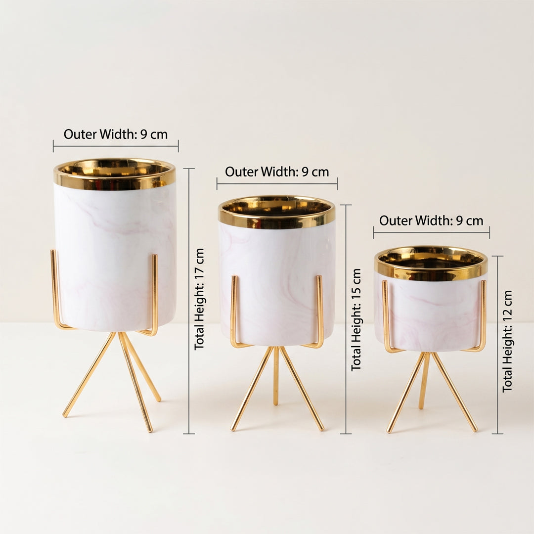 Three white marble-patterned cylindrical planters with gold metal rims and tripod stands, shown in different heights with overlaid dimension labels on a light neutral background.