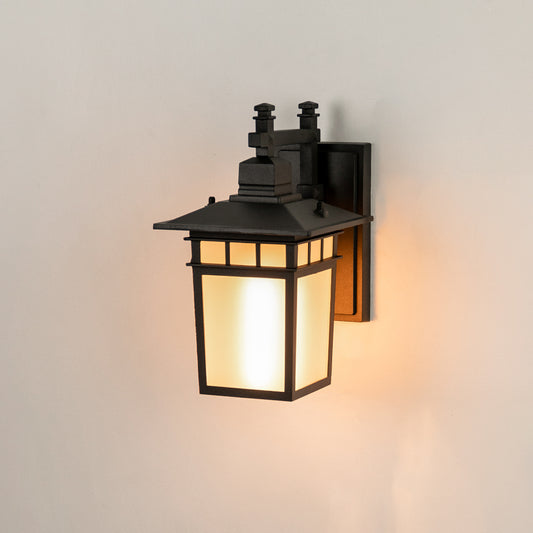 Modern black outdoor wall lantern on white background with a frosted glass shade casting a warm glow for entry decor.