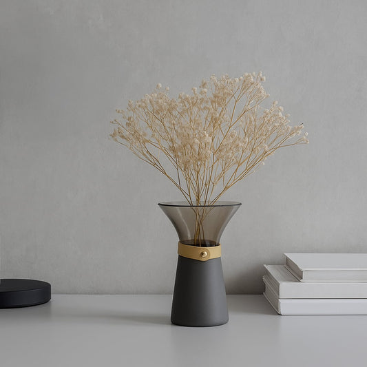 Minimal gray glass decorative vase with matte metal base placed on table holding dried beige florals for modern minimalist home decor.