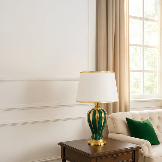 Table lamp with green and gold ceramic base and white shade styled for elegant modern home decor on a classic console.
