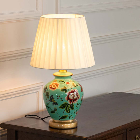 Green floral ceramic table lamp with pleated fabric shade creating refined traditional lighting on a wooden console table.