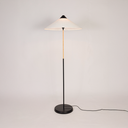 Floor lamp illuminated on clean white background showing tall sculpted base fabric drum shade and warm light output for modern home interiors.