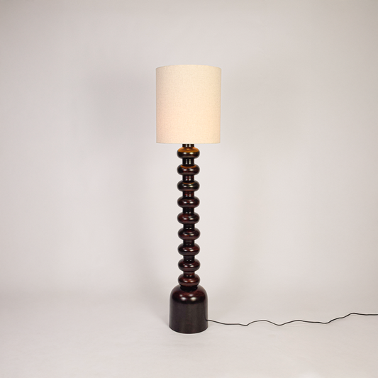 Floor lamp shown on clean white background with light on highlighting stacked sculpted base smooth finish and tall fabric shade for modern home decor.
