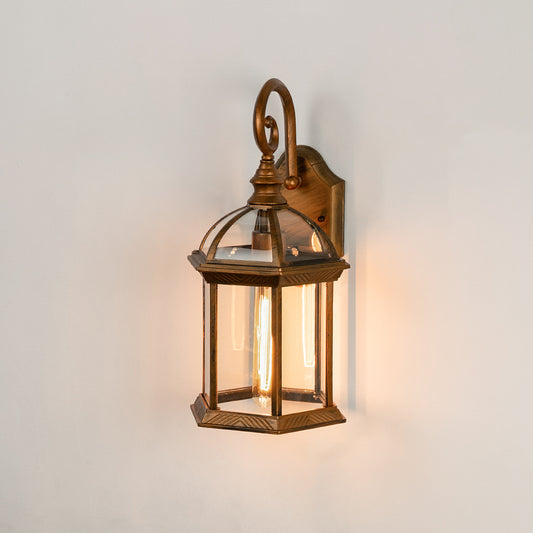 Antique brass metal outdoor wall light on white background with clear glass panels and an elegant top scroll arm design.