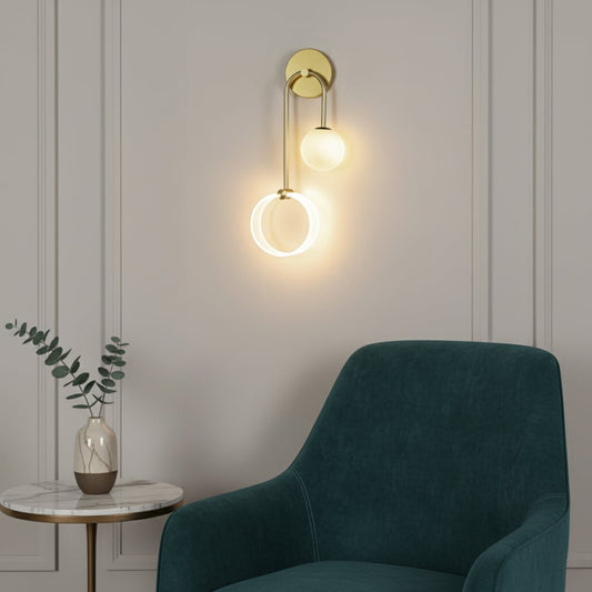 A modern wall light with glowing rings and a frosted globe mounted on a gold frame brightening a cozy room with a green chair and side table in a soft interior setting.