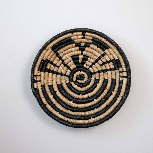 Handwoven seagrass round wall basket decor in natural beige and black with geometric spiral woven pattern on white background.