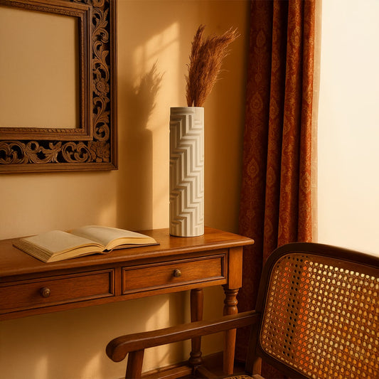 White geometric ceramic vase with embossed zigzag pattern placed on a wooden study desk beside an open book in a cozy vintage interior.