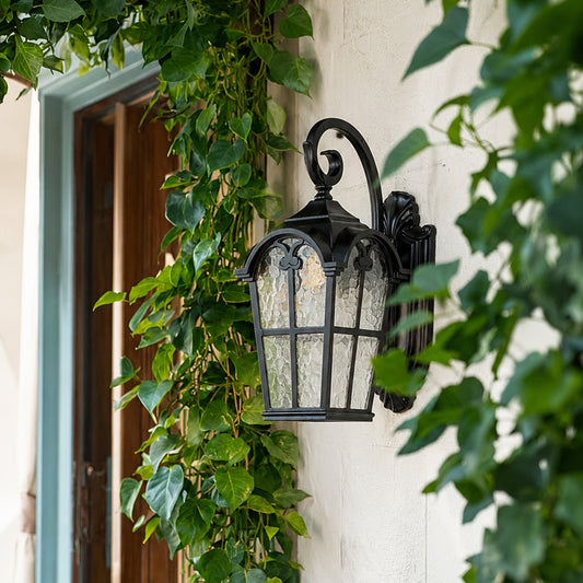 Black metal outdoor wall light lifestyle image with textured glass shade mounted on white villa wall with green ivy vines.