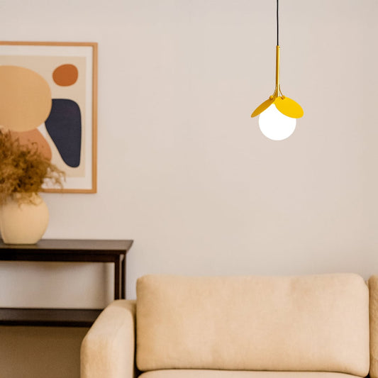 Pendant light with yellow frame and frosted globe glowing in modern living room decor above beige sofa.