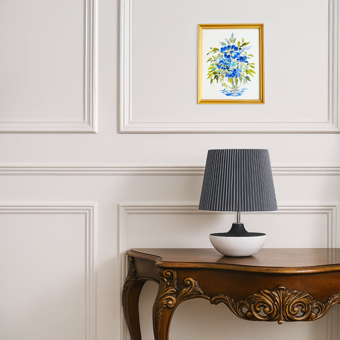 Modern table lamp with a black and white ceramic base and grey pleated shade placed on a carved wooden side table adding a soft contemporary touch to the room.