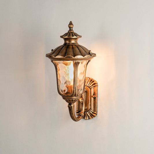 Antique brass outdoor wall lantern on white background with textured water glass shade for traditional porch decor.