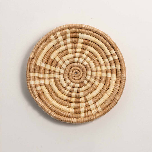 Round handcrafted natural brown cream woven seagrass wall basket with concentric spiral pattern on white background image.