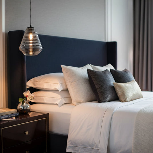 Glass pendant light in warm amber tone hanging beside bed adding soft ambient lighting and cozy elegance to modern bedroom decor.