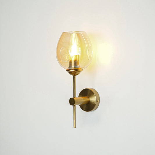 Contemporary brass wall light with amber glass globe for elegant bedroom and hallway decor.
