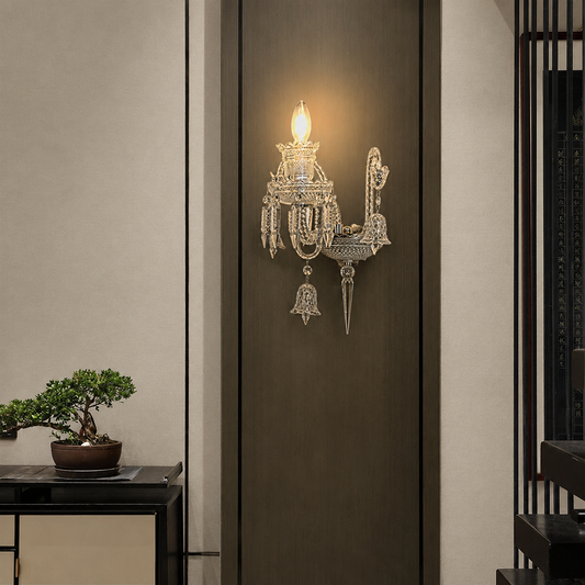 An ornate silver wall sconce with crystal-like hanging details and a glowing bulb, mounted on a dark brown door in a modern interior setting.