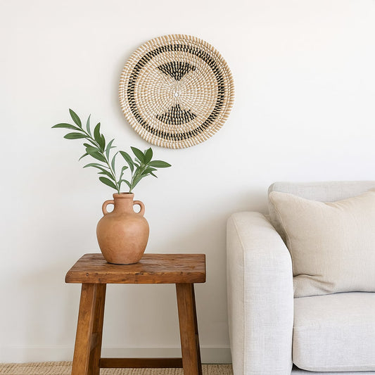 Decorative woven wall basket styled above a wooden side table beside a sofa creating a calm earthy accent for cozy interiors.