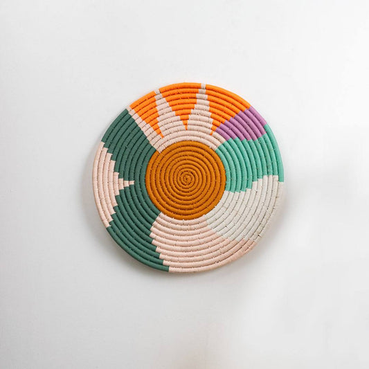 Round handcrafted multicolor seagrass wall basket with orange green cream and pink pattern on white background image.