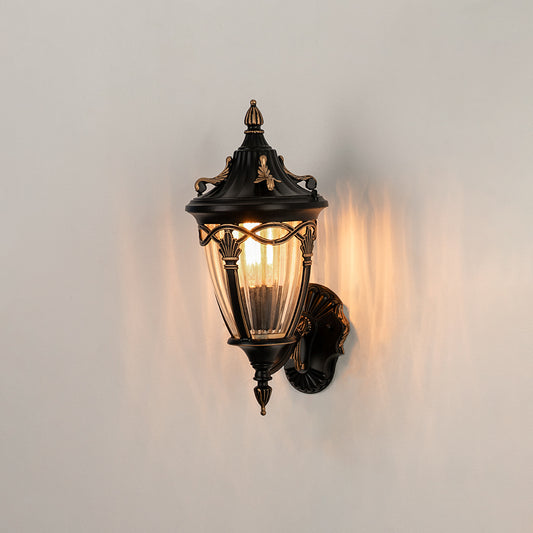 Antique bronze outdoor wall light on white background with ribbed glass shade casting a warm radial glow for patio decor.
