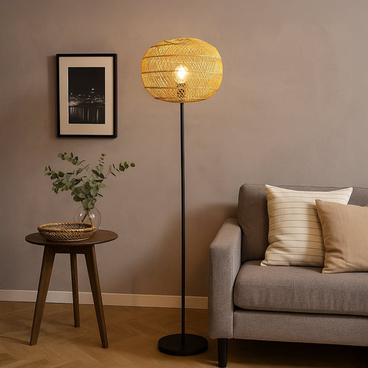 Black floor lamp with woven rattan shade beside grey sofa and wooden table in cozy modern living room.