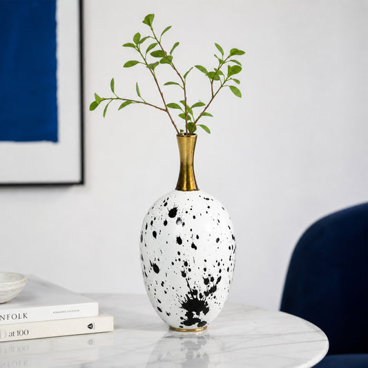 White and black ceramic flower vase with gold neck placed on marble table for elegant home decor.