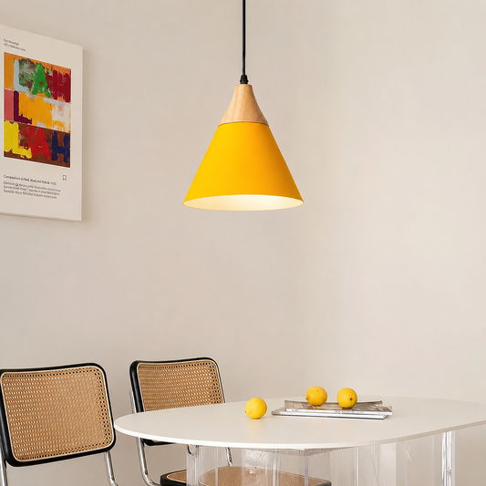 A modern pendant light with a bright yellow cone shade and a natural wood top, hanging above a white dining table with two woven-back chairs in a minimalist room.