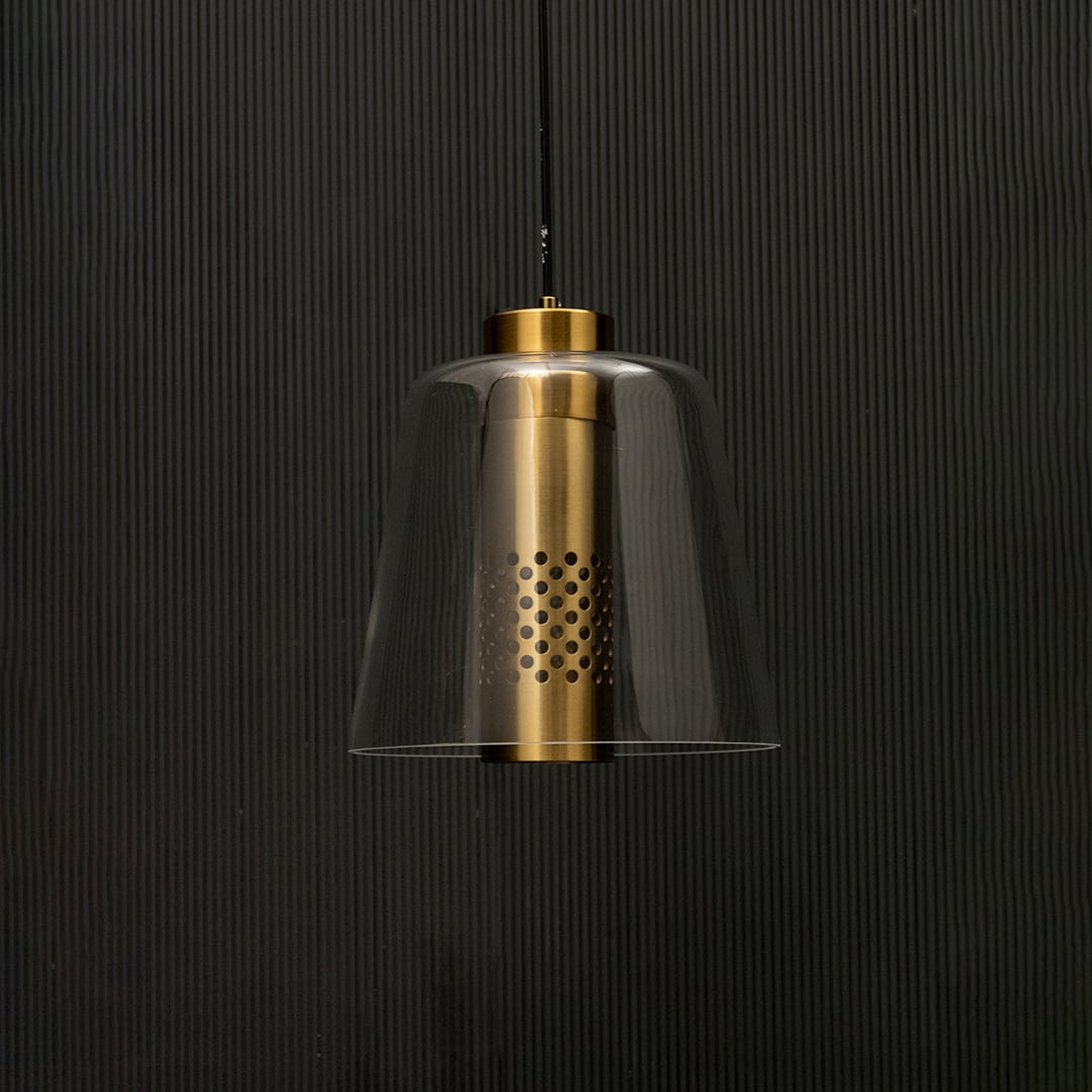 Brushed gold and clear glass pendant light with lights off on black background highlighting its elegant form and perforated metal centre.