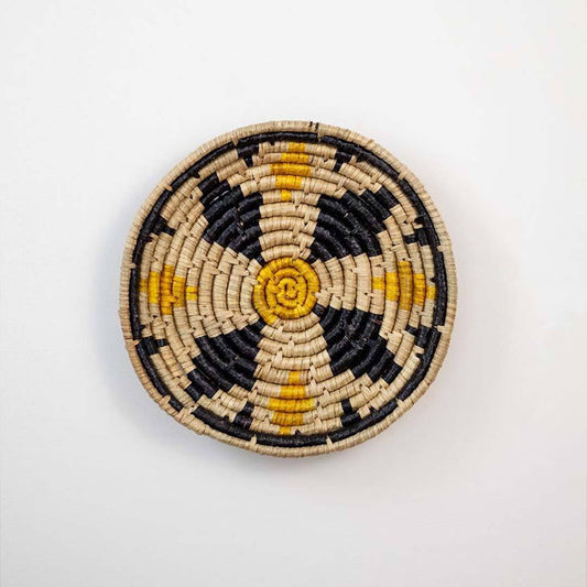 Handwoven seagrass round wall basket decor in natural beige black and mustard with floral woven pattern on white background.