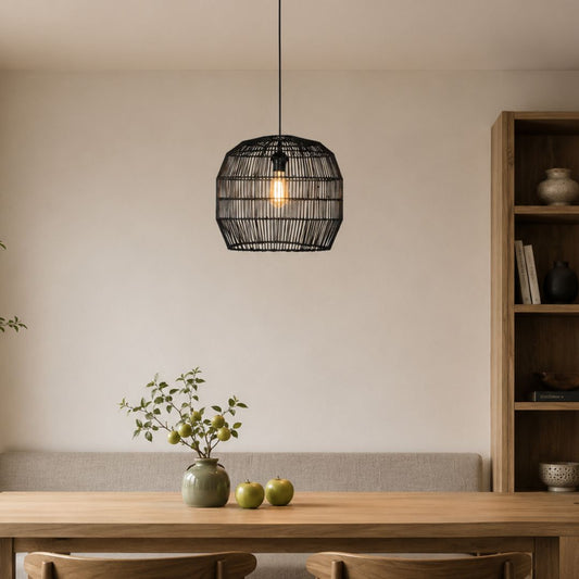 A black woven pendant light hangs over a wooden dining table in a minimalist room with a beige wall, a gray upholstered bench, and a wooden bookshelf.