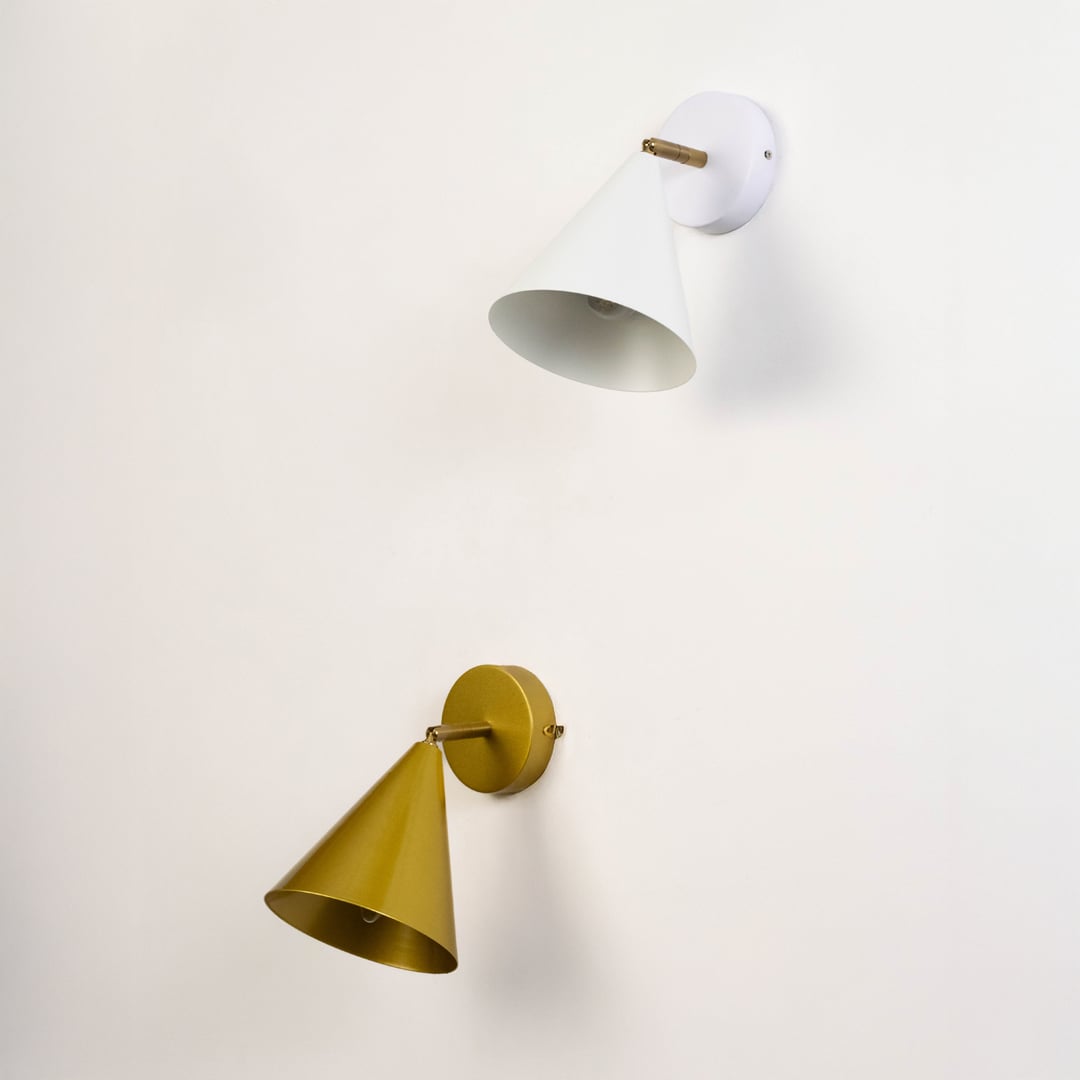 Two cone shaped wall sconces in white and gold mounted on a plain light wall with their shades angled downward.